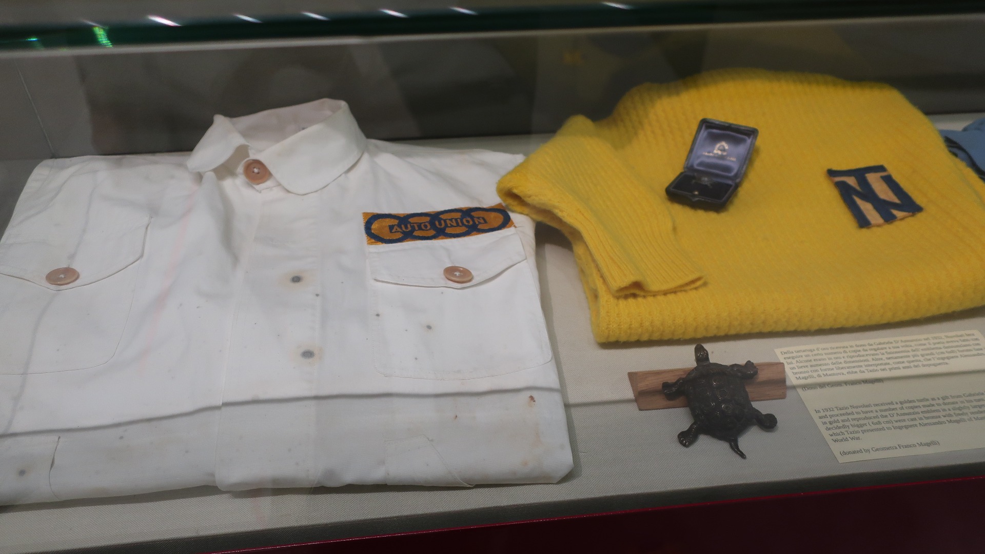 En overall fra Auto Union tiden, og en gul egendesignet skjorte med TN initialene, som Nuvolari designet selv. På løpsdagene foretrakk Tazio den gule skjorten.