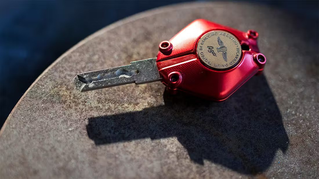 Den unike tenningsnøkkelen er utfrest av aluminum og eloksert i rødt, mens det runde feltet er en messingmynt laget av en av Agostinis egne pokaler.